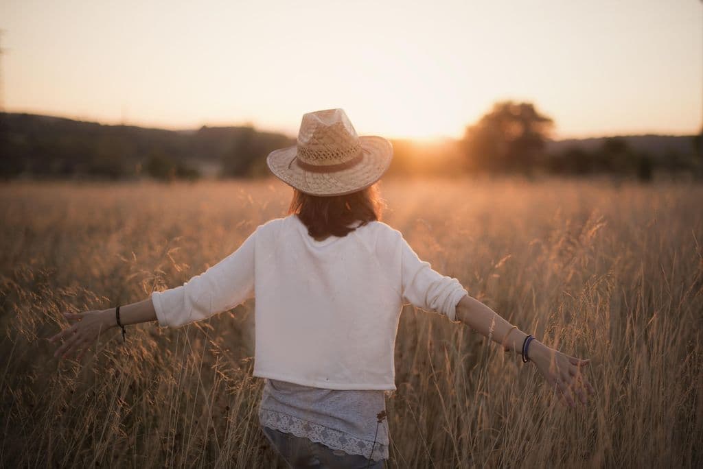 Une femme marchant dans un champ au coucher du soleil.